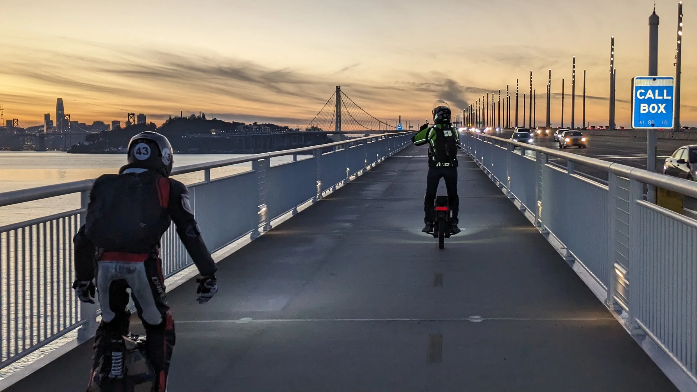Two EUC riders on the Bay Bridge bike path at sunset, the San Francisco skyline ahead