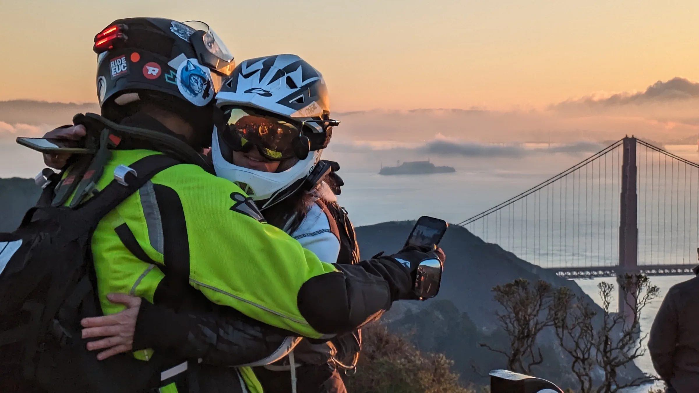 Two riders at a Marin Headlands overlook at sunset, the Golden Gate Bridge and a fog bank behind them